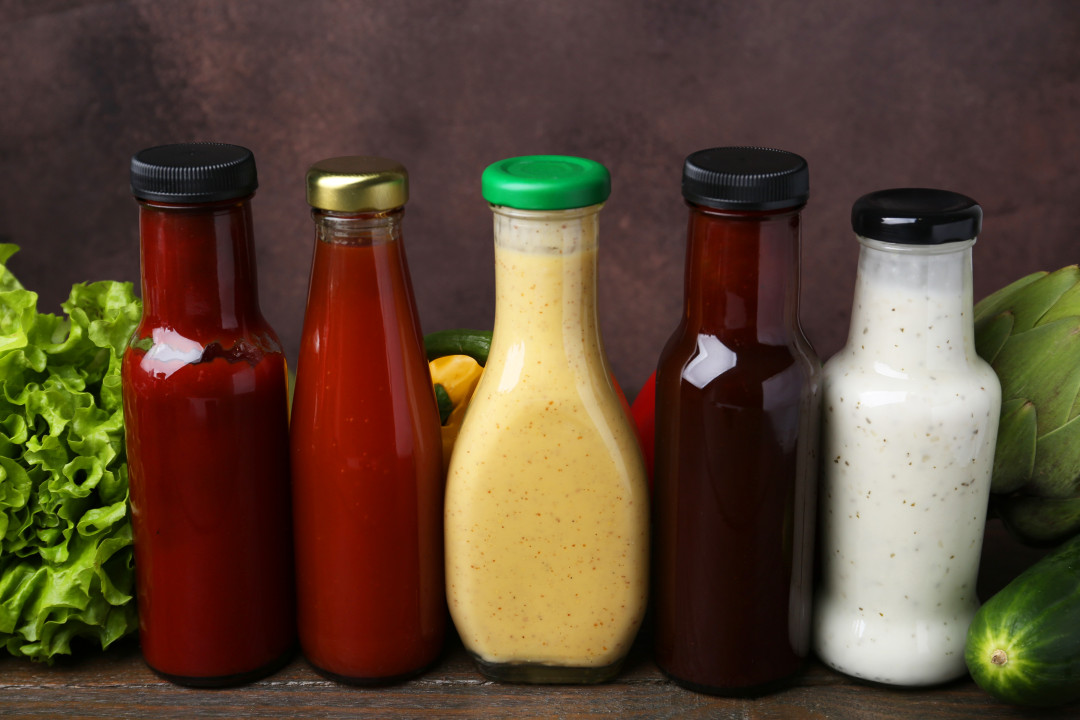Tasty sauces in glass bottles and fresh products on wooden table, closeup